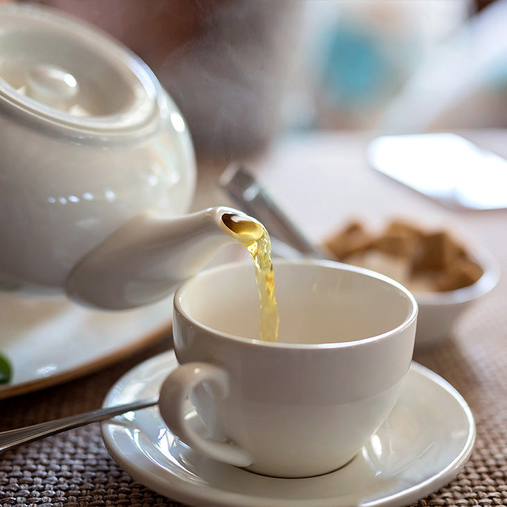 Tea is poured from a white teapot into a white teacup.